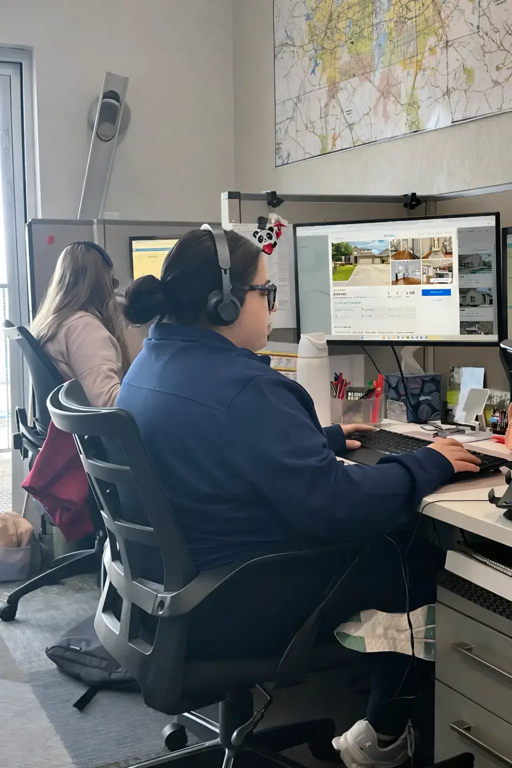 Two Home Services team members wearing headsets help clients set up utilities at a desk of computer monitors.