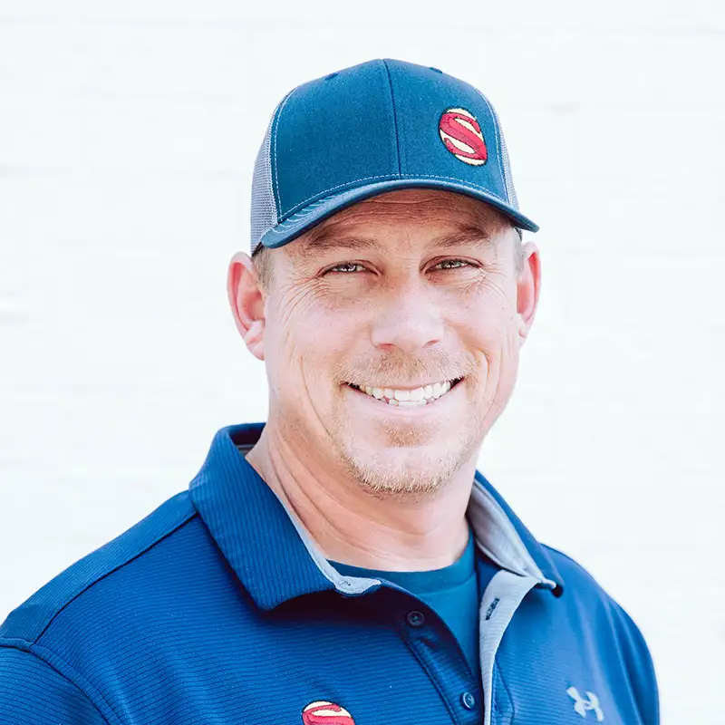 A man wearing a blue baseball cap and blue collared shirt with red S logos, smiling at the camera in front of a plain white background.